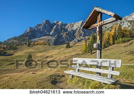 Stock Image - Wooden cross and bench, behind it the Eisenspitze, Dawin-Alpe, Strengen am Arlberg, Tyrol, Austria, Europe. Fotosearch