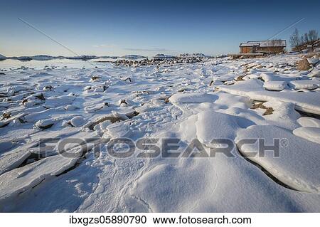 Stock Image - Wooden house on the beach, frozen fjord with ice floes in winter landscape, Nordland, Lofoten, Norway, Europe. Fotosearch
