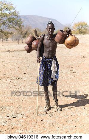 Stock Photograph - Young Himba man carries food on the cattle drive, Kaokoveld, Namibia, Africa. Fotosearch