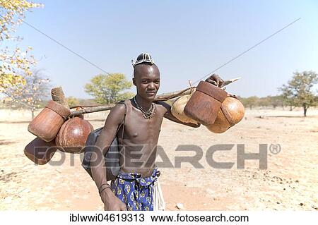 Stock Image - Young Himbamann carries water tank and food on the cattle drive, Kaokoveld, Namibia, Africa. Fotosearch