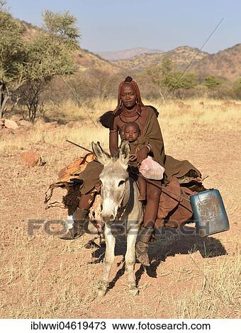 Stock Image - Young, married Himbafrau rides with a small child on a donkey, Kaokoveld, Namibia, Africa. Fotosearch