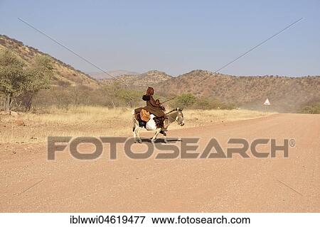 Stock Photo - Young, married Himbafrau rides with a small child on a donkey, Kaokoveld, Namibia, Africa. Fotosearch