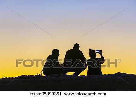 Young woman and men, twilight, talking, taking pictures with smartphone Baden-Württemberg, Germany, Europe View Large Photo Image Stock Image - Young woman and men, twilight, talking, taking pictures with smartphone Baden-Württemberg, Germany, Europe. Fotosearch