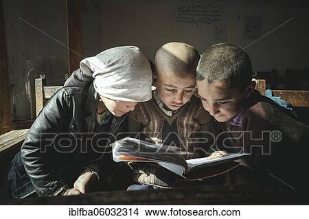 Picture - A girl and two boys reading a primer on a school desk, Potokh Primary School, Potokh, Wakhan Corridor, Afghanistan, Asia. Fotosearch