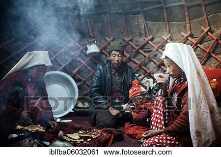 Stock Image - A man, two woman, a child at mealtime, nomadic Kyrgyz, yurt, a woman drinking milk tea from a bowl, Bozai Gumbaz, Wakhan Corridor, Badakhshan, Afghanistan, Asia. Fotosearch