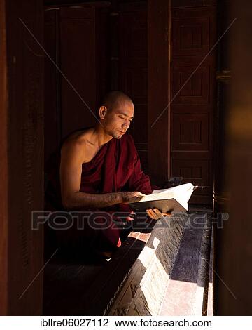 Stock Image - Buddhist monk in red robe reading ancient scriptures in a pagoda, Shwe Hin Thar Monastery, Sagaing, Myanmar, Asia. Fotosearch