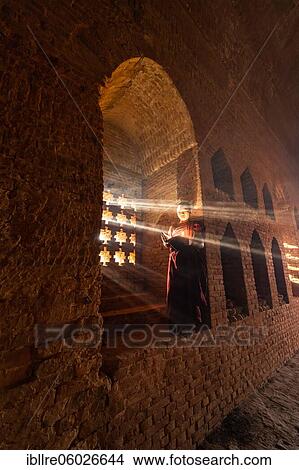 Buddhist young monk in red robe reading standing in front of rays of light in a temple, Bagan, Myanmar, Asia View Large Photo Image Picture - Buddhist young monk in red robe reading standing in front of rays of light in a temple, Bagan, Myanmar, Asia. Fotosearch