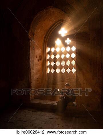 Buddhist young monk in red robe reading sitting in front of rays of light in a temple, Bagan, Myanmar, Asia View Large Photo Image Stock Image - Buddhist young monk in red robe reading sitting in front of rays of light in a temple, Bagan, Myanmar, Asia. Fotosearch