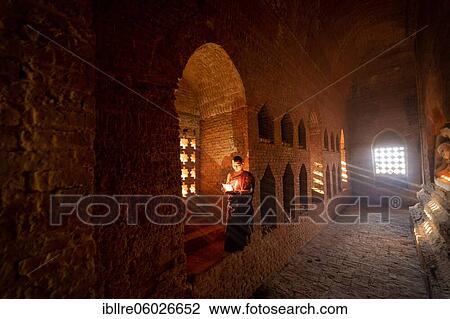 Buddhist young monk in red robe reading standing in front of rays of light in a temple, Bagan, Myanmar, Asia View Large Photo Image Stock Image - Buddhist young monk in red robe reading standing in front of rays of light in a temple, Bagan, Myanmar, Asia. Fotosearch