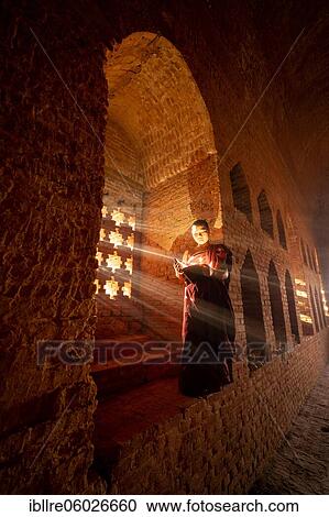 Buddhist young monk in red robe reading standing in front of rays of light in a temple, Bagan, Myanmar, Asia View Large Photo Image Stock Image - Buddhist young monk in red robe reading standing in front of rays of light in a temple, Bagan, Myanmar, Asia. Fotosearch