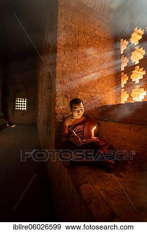 Stock Photo - Buddhist young monk in red robe reading sitting in front of rays of light in a temple, Bagan, Myanmar, Asia. Fotosearch