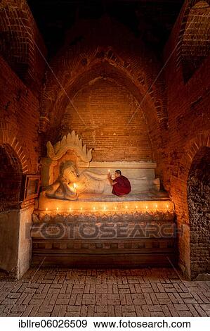 Stock Photo - Buddhist young monk in red robe with red umbrella praying with candle in hand in a temple, Bagan, Myanmar, Asia. Fotosearch
