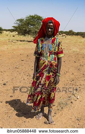 Stock Photo - Colourful dressed woman travels with a caravan of Peul nomads and their animals in the Sahel of Niger. Fotosearch