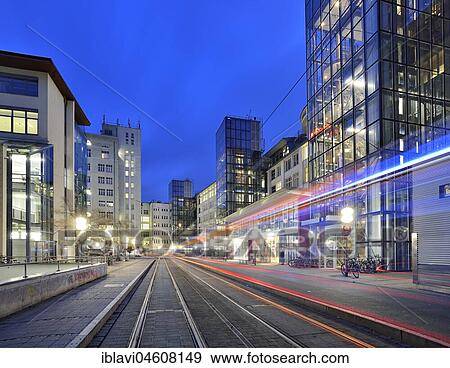 Stock Photo - Ernst-Abbe-Platz with traces of light from the tram at dusk, high-rise buildings, glass facades, Jena, Thuringia, Germany, Europe. Fotosearch