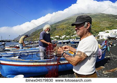 Stock Image - Fishermen repair nets at Scari Beach, in the background of the volcano, Stromboli Island, Lipari Islands, Italy, Europe. Fotosearch