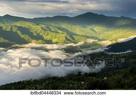 Picture - Fog is covering Phewa Lake in the morning, surrounding hills with trees are sunlit, Sarangkot, Kaski District, Nepal, Asia. Fotosearch