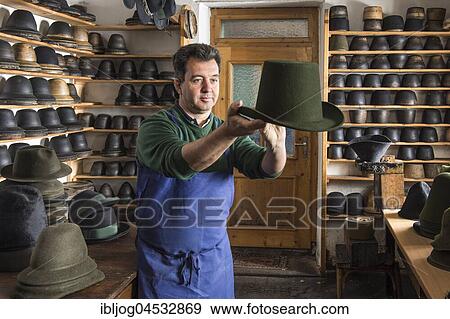 Stock Photo - Hatter examining finished wool felt hat, hat molds on wooden shelves and finished hats behind, hatmaker workshop, Bad Aussee, Styria, Austria, Europe. Fotosearch