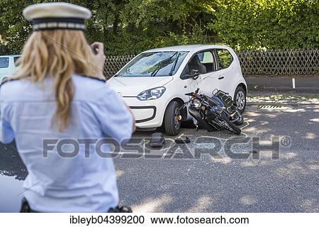 Stock Image - Heavy road accident, Simson scooter crashing in car, policewoman recording accident, Germany, Europe. Fotosearch