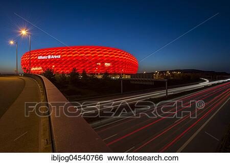 Stock Photograph - Illuminated Allianz Arena in red with light trails of driving cars, time exposure, twilight, Munich, Bavaria, Germany, Europe. Fotosearch