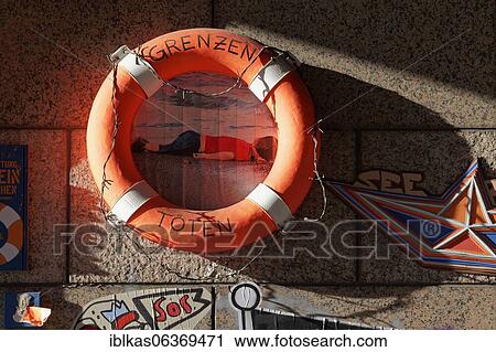 Stock Image - Lifebelt with writing Killing borders, art object on the subject of sea rescue at a wall, open-air gallery Flingern, Düsseldorf, North Rhine-Westphalia, Germany, Europe. Fotosearch
