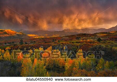 Stock Image - Low clouds, storm clouds glow in the evening light, mountainous landscape, dramatic light above autumn forest, Dallas Divide, Colorado, USA, North America. Fotosearch
