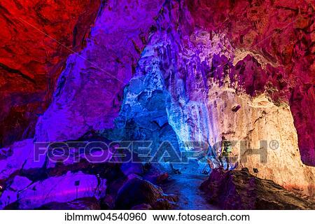 Stock Image - Man in a colourfully illuminated stalactite cave with stalagmites and stalactites, Nebelhöhle, Sonnenbühl, Baden-Württemberg, Germany, Europe. Fotosearch