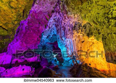 Stock Image - Man in a colourfully illuminated stalactite cave with stalagmites and stalactites, Nebelhöhle, Sonnenbühl, Baden-Württemberg, Germany, Europe. Fotosearch