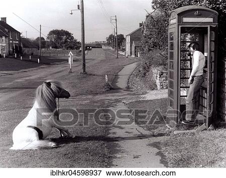 Stock Photo - Man on the phone in a payphone box. His pony is waiting, England, Great Britain.. Fotosearch