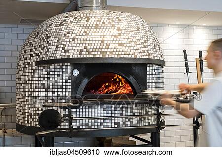 Stock Image - Man putting a pizza into modern Italian pizza stove. Fotosearch