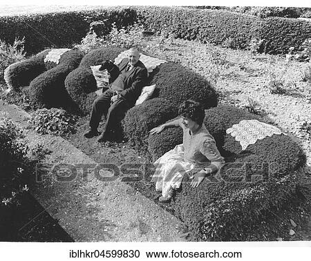 Stock Image - Old couple sitting on an armchair from a hedge, England, Great Britain. Fotosearch