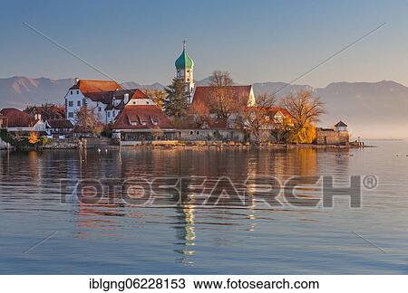 Stock Image - Peninsula with the parish church of St. George in front of the Alps in the evening sun, moated castle on Lake Constance, Swabia, Bavaria, Germany, Europe. Fotosearch
