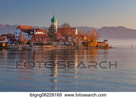 Stock Photo - Peninsula with the parish church of St. George in front of the Alps in the evening sun, moated castle on Lake Constance, Swabia, Bavaria, Germany, Europe. Fotosearch