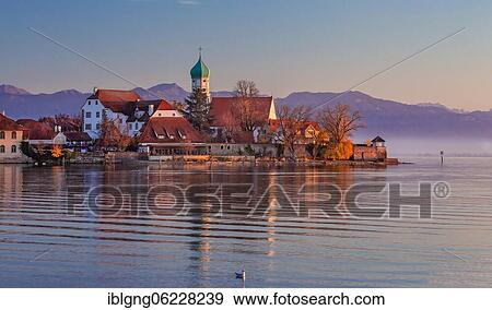 Stock Photo - Peninsula with the parish church of St. George in front of the Alps in the evening sun, moated castle on Lake Constance, Swabia, Bavaria, Germany, Europe. Fotosearch