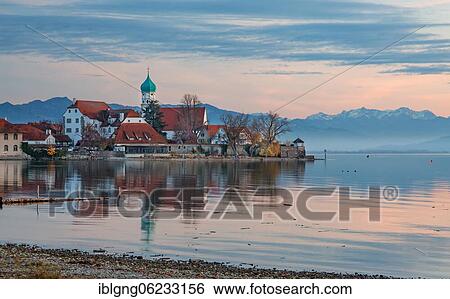 Stock Photograph - Peninsula with the parish church of St. George in front of the Alps in the evening sun, moated castle on Lake Constance, Swabia, Bavaria, Germany, Europe. Fotosearch