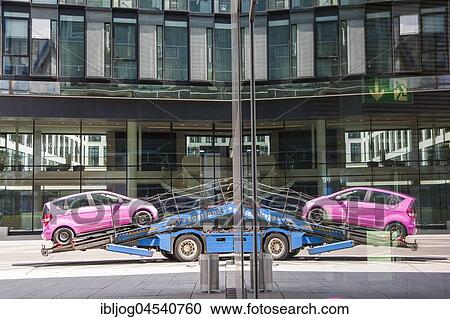 Stock Image - Reflection, pink car standing on car transporter, reflection in glass facade, Munich, Bavaria Germany. Fotosearch