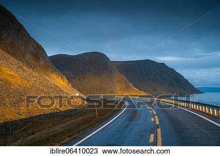 Stock Image - Road leading to rainbow with dramatic sky and sunset light, Sarnes, North Cape, Norway, Europe. Fotosearch