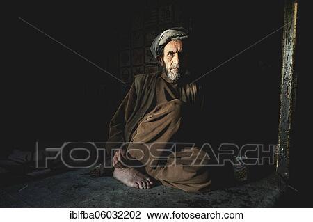 Stock Image - Shopkeeper sitting in the semi-darkness on the floor of his shop, Ishkashim, Afghanistan, Asia. Fotosearch