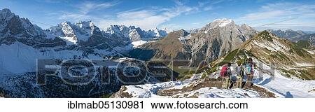 Stock Image - Three hikers on hiking trail with snow in autumn, hike to the summit of the Hahnenkampl, view of snow-covered peaks Laliderspitze, Dreizinkenspitze and Spritzkarspitze, behind Gamsjoch and Gramaijoch, Engtal, Karwendel, Tyrol, Austria, Europe. Fotosearch