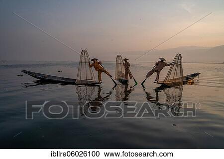 Stock Image - Three traditional fishermen pose standing on their small boats, at sunrise, Lake Inle, Myanmar, Asia. Fotosearch