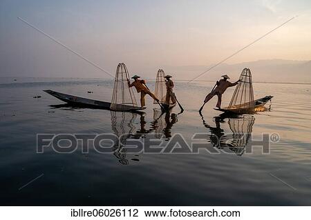 Stock Image - Three traditional fishermen pose standing on their small boats, at sunrise, Lake Inle, Myanmar, Asia. Fotosearch
