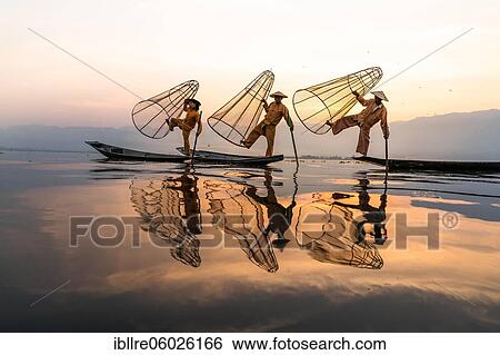 Stock Photograph - Three traditional fishermen pose standing on their small boats, at sunrise, Lake Inle, Myanmar, Asia. Fotosearch