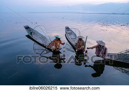 Stock Photography - Three traditional fishermen sitting with lamps on their small boats, at sunrise, Lake Inle, Myanmar, Asia. Fotosearch