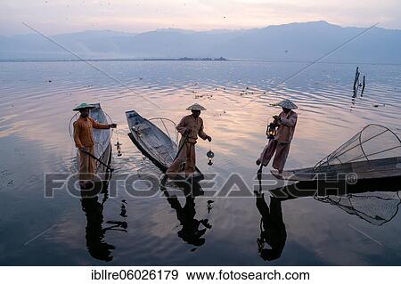 Stock Photo - Three traditional fishermen stand with lamps on their small boats, at sunrise, Lake Inle, Myanmar, Asia. Fotosearch