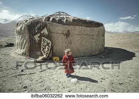 Stock Image - Three-year-old girl in traditional traditional traditional traditional traditional traditional traditional traditional traditional traditional costume, nomadic Kyrgyz, behind her traditional yurt, which is being dismantled, Bozai Gumbaz plateau,.... Fotosearch