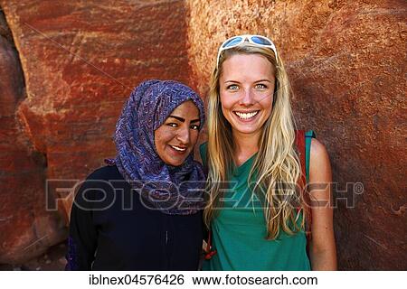 Stock Photograph - Tourist girl poses with local bedouin girl at colourful rock-formations in Petra, Wadi Musa, Jordan, Asia. Fotosearch