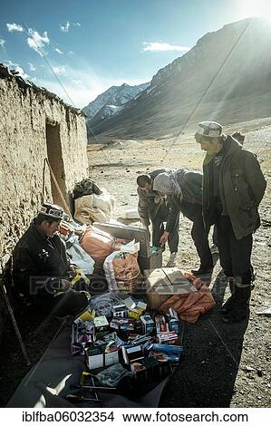 Picture - Trader spreads electronics, medicines, batteries, clothes and tools on the floor in front of a stone house in front of three men, Khadz Goz, Wakhan Corridor, Badakhshan, Afghanistan, Asia. Fotosearch