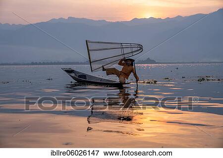 Stock Photo - Traditional fisherman poses sitting on his small boat in front of sunrise, Lake Inle, Myanmar, Asia. Fotosearch