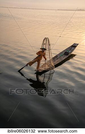 Stock Image - Traditional fisherman posing standing on his small boat in front of sunrise, Lake Inle, Myanmar, Asia. Fotosearch