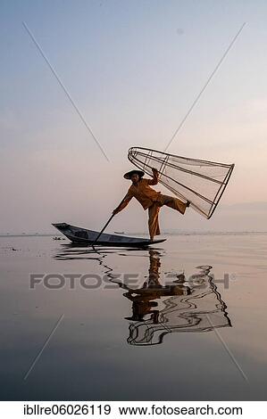 Stock Photo - Traditional fisherman posing standing on his small boat with reflection in front of sunrise, Lake Inle, Myanmar, Asia. Fotosearch