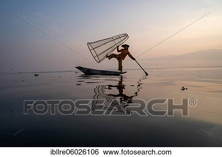 Traditional fisherman posing standing on his small boat with reflection in front of sunrise, Lake Inle, Myanmar, Asia View Large Photo Image Stock Photograph - Traditional fisherman posing standing on his small boat with reflection in front of sunrise, Lake Inle, Myanmar, Asia. Fotosearch